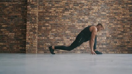 Wall Mural - A side view of a focused man is doing stretching exercises standing isolated over a brick wall