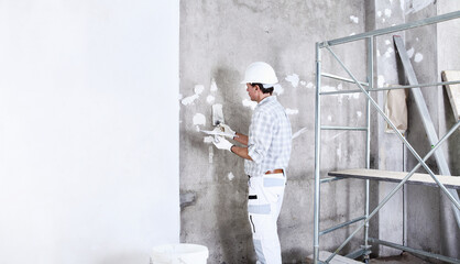 Wall Mural - plasterer man at work with trowel plastering the wall of interior construction site wear helmet and protective gloves, scaffolding on background and copy space on white wall