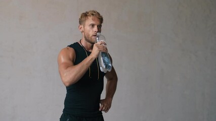 Wall Mural - A muscular blonde man is drinking water standing in the studio