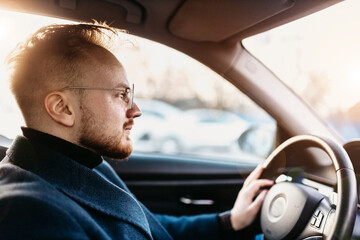 Wall Mural - male driver in business attire drives a car in winter on a sunny day. business trip behind the wheel