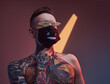 © Fxquadro - Weared with protective black mask stylish hipster guy with modern hairstyle and naked torso poses in dark and colourful room showing his tattooed body.