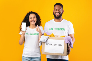 Wall Mural - Two Volunteers Holding Donation Box Showing Phone Screen, Yellow Background