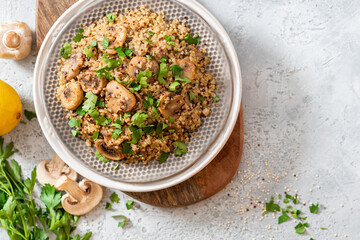 Wall Mural - Quinoa stewed with mushrooms, onions, garlic, and parsley in a plate on a gray concrete background top view. Delicious and healthy vegetarian food. Quinoa with champignons.