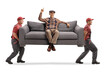 Movers carrying an elderly man sitting on a sofa and pointing up