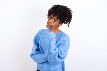 Wall Mural - Young beautiful African American woman wearing blue knitted sweater against white wall Pointing to the eye watching you gesture, suspicious expression.