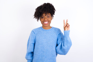 Wall Mural - Young beautiful African American woman wearing blue knitted sweater against white wall showing and pointing up with fingers number two while smiling confident and happy.