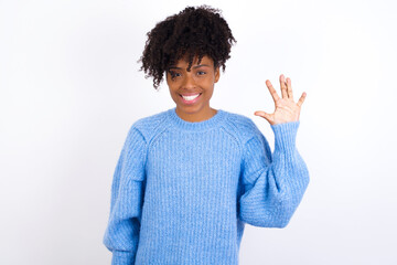 Wall Mural - Young beautiful African American woman wearing blue knitted sweater against white wall showing and pointing up with fingers number five while smiling confident and happy.