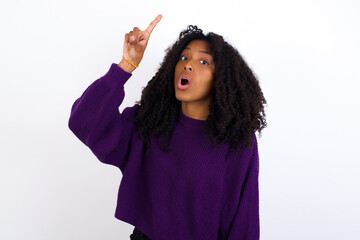 Wall Mural - Young beautiful African American woman wearing knitted sweater against white wall, pointing finger up and looking inspired by genius thought, showing good idea sign, having clever solution in mind