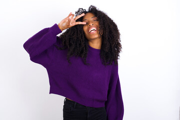 Wall Mural - Young beautiful African American woman wearing knitted sweater against white wall, Doing peace symbol with fingers over face, smiling cheerful showing victory