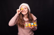 © Vulp - Young pretty girl holding a box with macaroons, and covering one eye, over black background is smiling at the camera.
