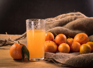 Fresh juicy tangerines or mandarins with green leaves on sack cloth and wooden table and glass of fresh juice.