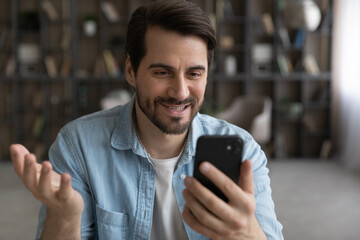Wall Mural - smiling young caucasian man look at smartphone screen talk on video call on modern gadget. happy mil