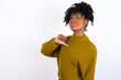 Closeup of cheerful Young beautiful African American woman wearing knitted sweater against white wall looks joyful, satisfied and confident, points at himself with thumb.