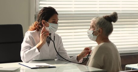 Wall Mural - Doctor use stethoscope checking up heart beat rate of older female patient, writes results fill medical history card at meeting in hospital. Medical checkup, care of senior clients, cardiology concept