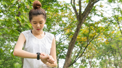 Asian cute healthy fit and firm slim teen lady look at the smartwatch to set GPS or heart rate before running and workout  at outdoor garden park