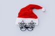 © Limages Studio - Red Santa Claus hat with festive glasses on gray background, top view