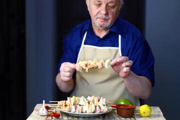 Senior man chef prepares chicken skewers on wooden sticks. Cooking kebabs.