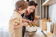 Candid Family in the kitchen. Mother and son baking carrot cake together. Scandinavian kitchen interior. Mom helps and teaches her son how to decorate a cake. Little assistant on kitchen