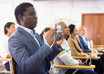 African american man attending business event recording lecture on smartphone at conference hall