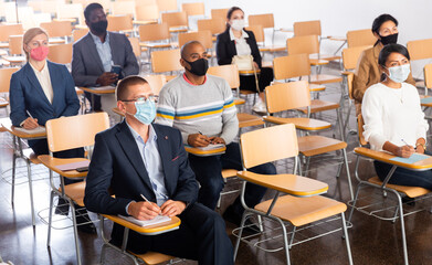 Wall Mural - Multiethnic group of people wearing protective masks sitting in conference room keeping distance during business training. Precautions during mass events in coronavirus pandemic