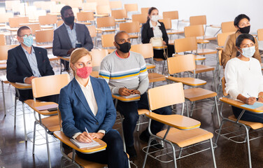 Canvas Print - International group of business people wearing protective face masks listening to presentation in conference room. Concept of precautions and social distancing in COVID 19 pandemic