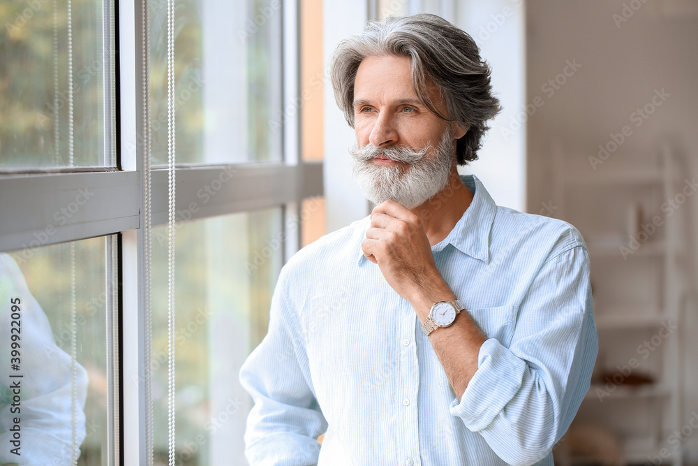 Mature man with grey hair near window at home