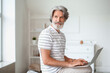© Pixel-Shot - Mature man with laptop sitting on sofa at home
