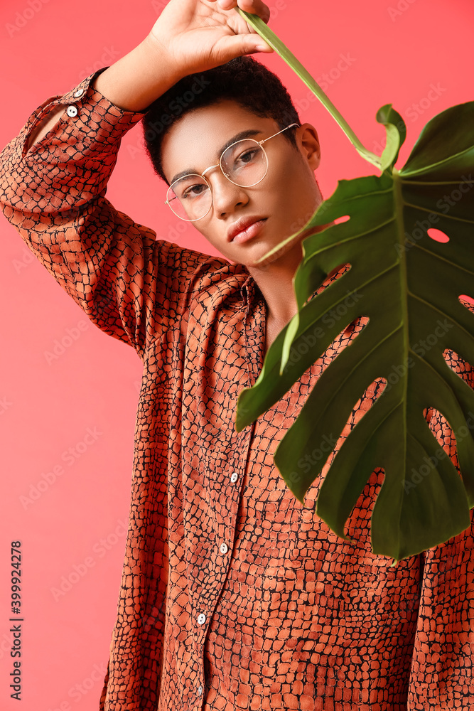 Stylish young African-American man with tropical leaf on color background