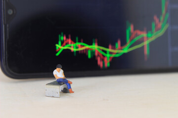 Wall Mural - Simple Conceptual Photo, illustration for Young Man Investor Mini Figure Toy businessman Seriously watching Running Stock Exchange Sitting at stappler