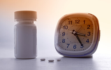 White sleeping pills lying near an analogic alarm clock. Insomnia concept