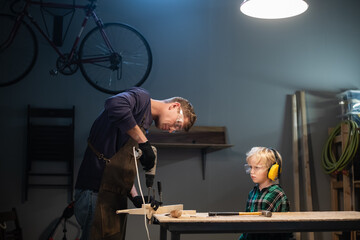 an experienced carpenter shows the work of various tools to his son in the workshop