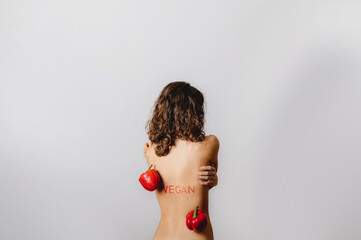 Copy space vertical close-up naked back of woman portrait raising arms with red vegan write and two sweet peppers. Womanly, healthy lifestyle, diet, vegan and vegetarian concept.