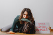 © Pintau Studio - Portrait with attractive woman and puppy lying on the ground. Dog bites a carrot and Lady eats a green leaf while showing a protest sign with the slogan stop eating animal. Vegan, vegetarian concept.