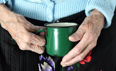 Wall Mural - In her hands, an old grandmother of 90 years holds in her hand a metal mug with water, poverty and misery, the hunger of the older generation.