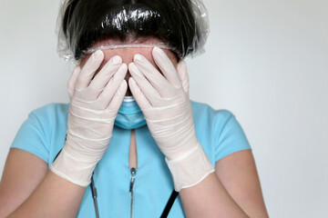 Woman in medical mask and latex gloves covers her face with hands. Upset or tired doctor after hard work, concept of covid-19 coronavirus treatment