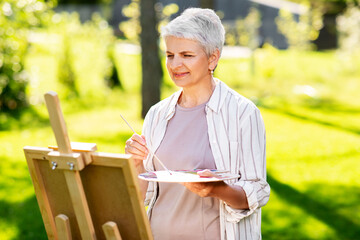 Canvas Print - creativity, art and hobby concept - senior woman with easel and color palette painting outdoors