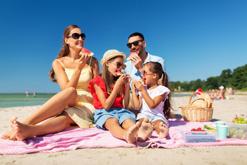 Wall Mural - family, leisure and people concept - happy mother, father and two daughters having picnic on summer beach and eating watermelon