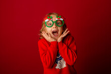Little Girl In Carnival Glasses Holds A Gift On A Red Background, Christmas