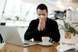 © Ivan - Sick man with runny nose came working in coffee shop. Tired man in black shirt blows his nose in public place. Isolate yourself if you get sick. Stay home concept. Cup of coffee and laptop on table.