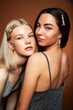 © iordani - two pretty diverse girls happy posing together: blond and brunette on brown background, lifestyle people concept