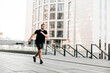 © Ivan - Young fit man doing urban running workout on asphalt road sprinting in sport and healthy lifestyle concept. Big city on background. Black sportswear. Caucasian man jogging.
