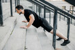 © Ivan - Well built young man pushing up from stairs. Side view. Athletic man with black hair wearing black sportswear and sneakers working out on street. Concentrated man excercising to have a fit body.