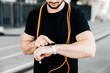 © Ivan - Athletic man with orange jumping rope around neck setting up his smart watch. Cut view of confitent male runner which records the results of the run on the device. Modern technologies concept.
