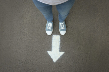 Wall Mural - Woman standing near arrow on asphalt, top view