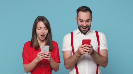 Wall Mural - Surprised young couple friends bearded man woman 20s wearing white red clothes posing isolated on blue background studio. People lifestyle concept. Using mobile cell phone typing sms message say wow