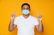 © Drobot Dean - Asian man in face mask looking at camera and pointing fingers upward
