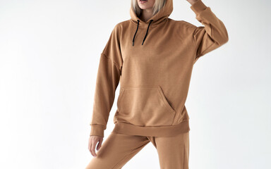 Wall Mural - girl wears light brown hoodie and pants. isolated photo of women wearing nude color fleece textile outfit.