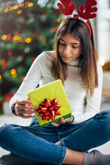 A cheerful teenage girl with deer antlers opening a Christmas present