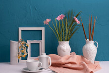 Dry Daffodils, Photo Frames, A Cup With Coffee And A Teapot And Two Vases With Gerbera Flowers On A Blue Background