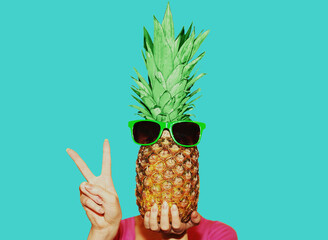 Stylish image of woman covering her face with pineapple with sunglasses isolated on a blue background